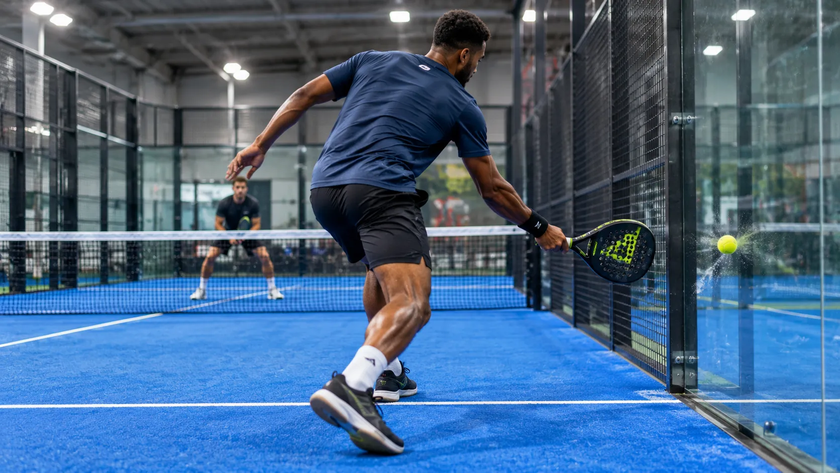 A padel player hitting the ball off the back glass wall while the opponent waits at the net.